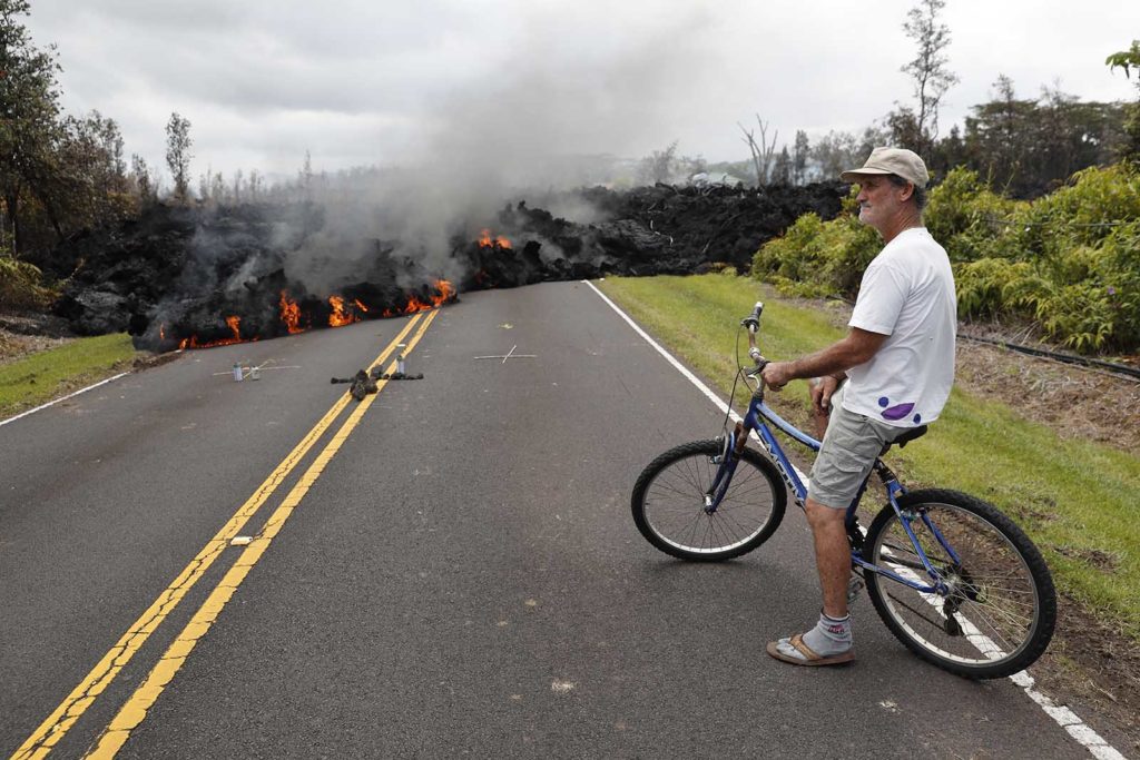 Leilani Estates resident Sam Knox watches the lava stretch across the road, Saturday, May 5, 2018, in Pahoa, Hawaii. Knox's home is less than a few hundred yards from the lava flow and he does not have any plans to evacuate. Knox is hopeful the lava will not take his home. (AP Photo/Marco Garcia)