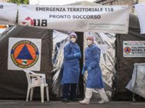 Two healthcare professionals wearing protective suits and healthcare masks walk in front of the advanced medical unit built up outside the emergency room of the Piacenza hospital to deal with the coronavirus emergency and to perform swabs, Piacenza 27 Febbraio 2020. Officials say that the number of people which have died due to the COVID-19 coronavirus in Italy has climbed to 12 while more than 400 persons have contracted the virus. ANSA/MATTEO CORNER