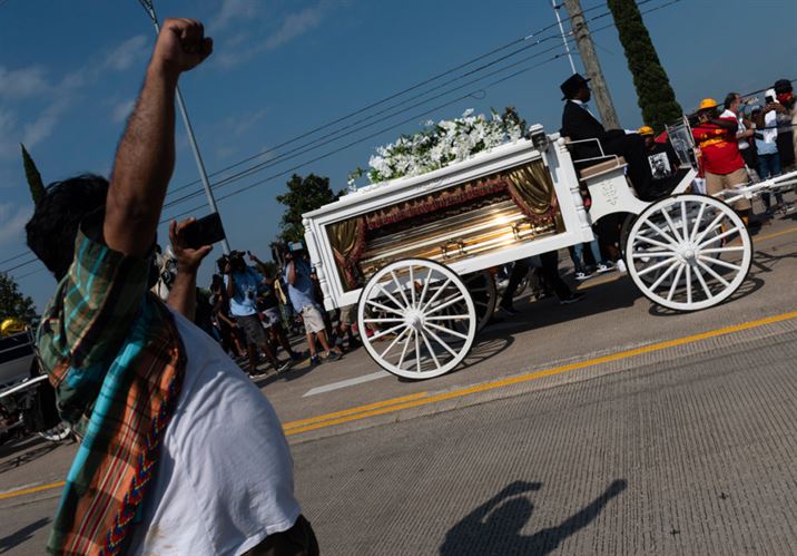 A man raises his fist as mourners watch the casket of George Floyd carried by a white horse-drawn carriage to his final resting place at the Houston Memorial Gardens cemetery in Pearland, Texas on June 9, 2020. - George Floyd will be laid to rest Tuesday in his Houston hometown, the culmination of a long farewell to the 46-year-old African American whose death in custody ignited global protests against police brutality and racism. Thousands of well-wishers filed past Floyd's coffin in a public viewing a day earlier, as a court set bail at $1 million for the white officer charged with his murder last month in Minneapolis. (Photo by ANDREW CABALLERO-REYNOLDS / AFP)